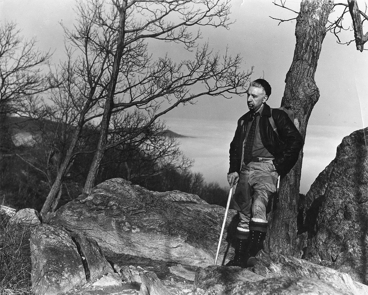 Early hiker with walking stick leans on blazoned tree (Courtesy of the Appalachian Trail Conservancy)